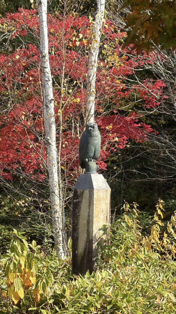 【画像:白樺と紅葉を背にしたフクロウの像】