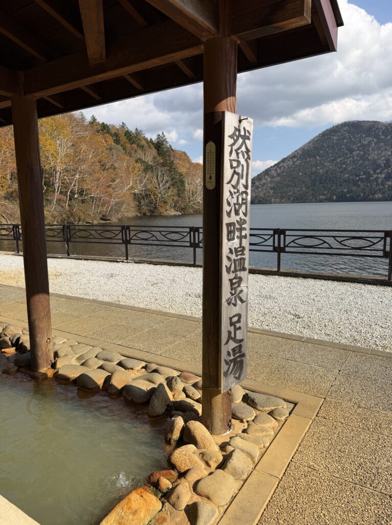 【画像:然別湖畔温泉 足湯の看板と湖の眺め】